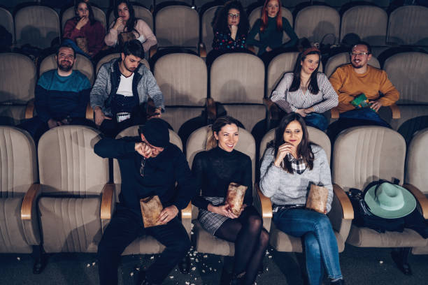 Group of young people sitting in modern cinema and watching funny movie. They are happy and laughing.