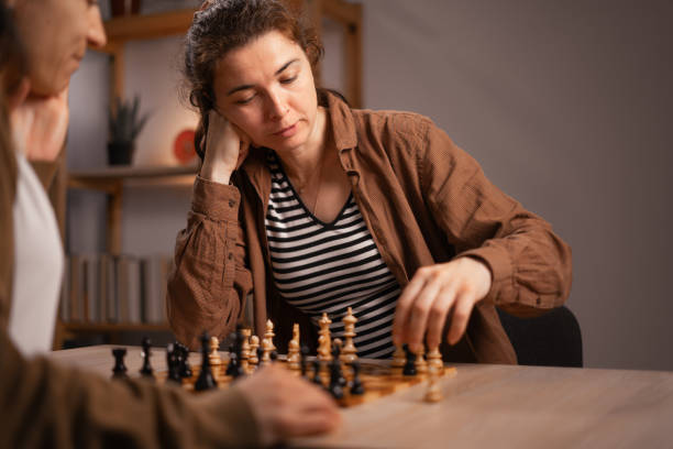 Two women sit at a table play chess at home in the evening. intellectual engagement and social in board games