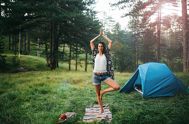 Vintage toned image of a young woman relaxing and practicing morning yoga exercise in the forest, while camping in the beautiful outdoors of the Dinaric Alps in the Southeastern Europe. The sun rays are coming through the woods, creating an idyllic moment in the nature.