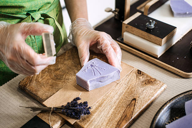 Hands pressing a floral stamp onto handmade lavender soap bar. Focus on natural skincare, organic soap making, and sustainable living practices.