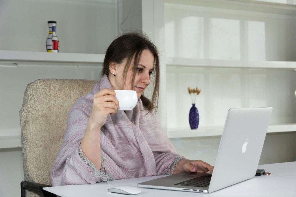 Woman wrapped in a cozy shawl, drinking coffee while working on a laptop — representing a calm rainy-day routine.