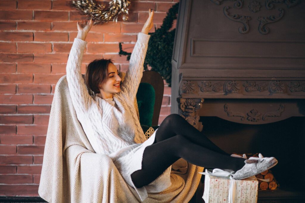 A woman enjoying a cozy and relaxing morning routine, smiling and stretching in a warm room — symbolizing morning routine ideas that make you excited to wake up.