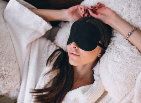 Woman relaxing on a bed while wearing a black eye cover for better sleep and comfort