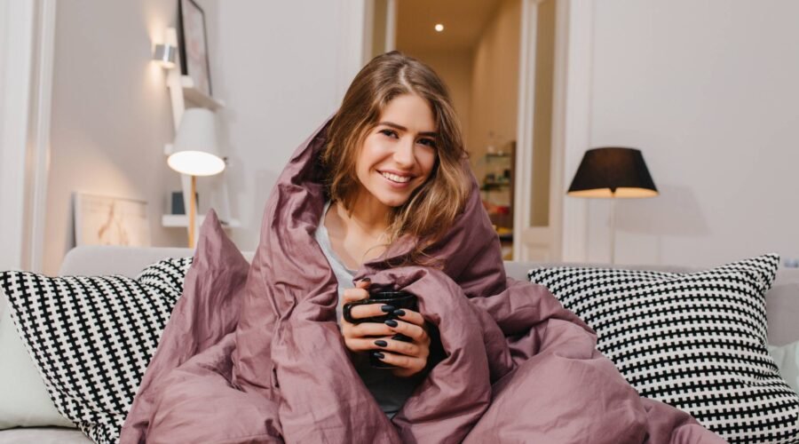 Woman wrapped in a cozy blanket holding a warm drink, enjoying a peaceful evening at home — perfect example of winter self care.