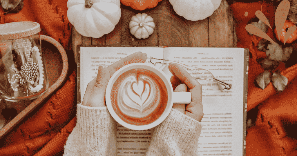 A girl holding a Starbucks Pumpkin Cream Cold Brew in a cozy setting with a book on the table.