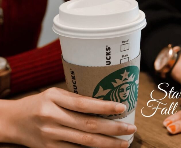 Person holding a Starbucks coffee cup on a table, representing the Starbucks Fall Menu.
