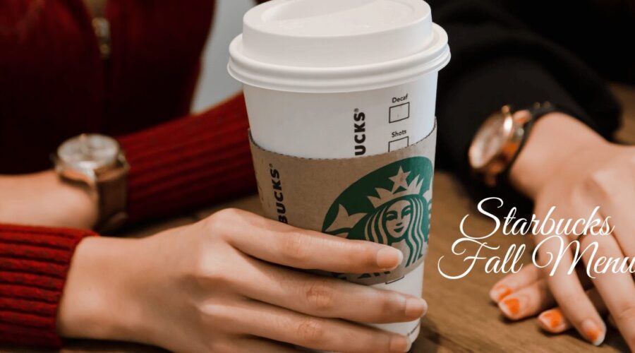 Person holding a Starbucks coffee cup on a table, representing the Starbucks Fall Menu.