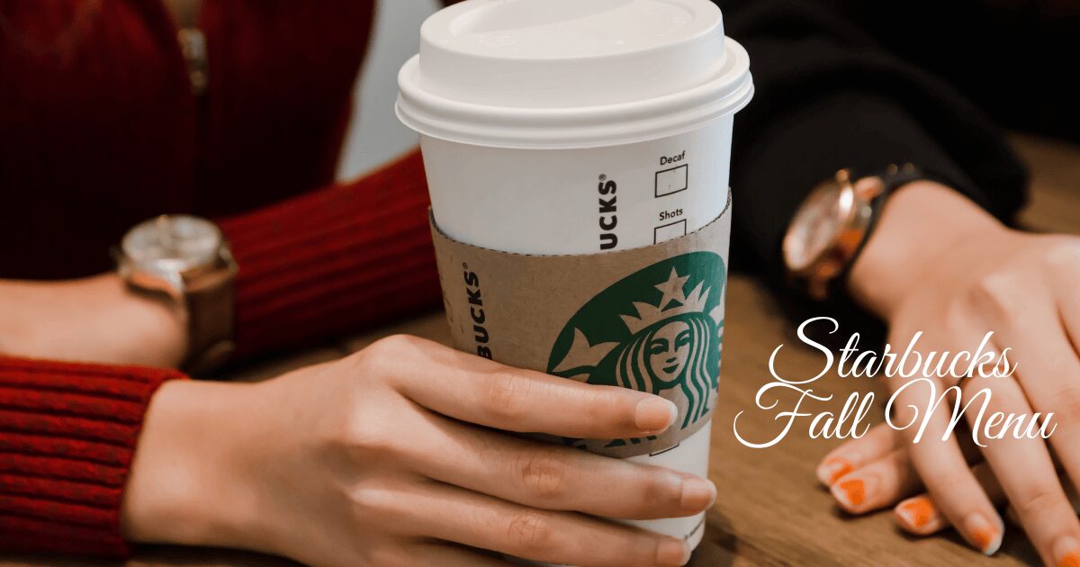 Person holding a Starbucks coffee cup on a table, representing the Starbucks Fall Menu.