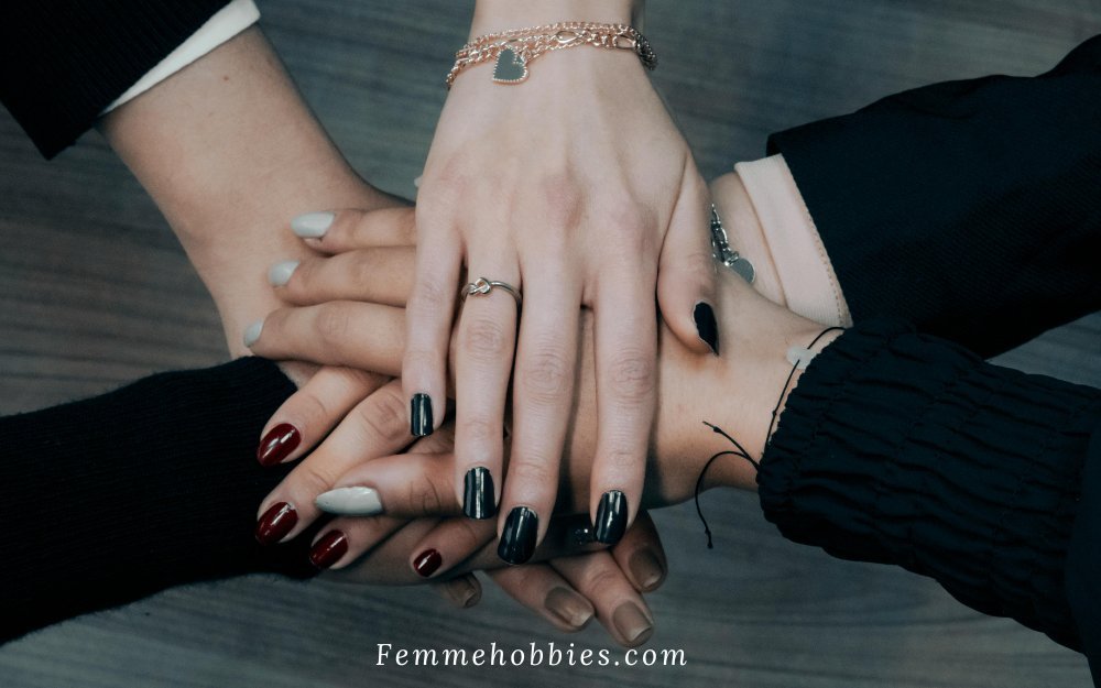 Hands layered together showcasing the core palette of fall nail colors, including deep burgundy, black, nude, and soft gray manicures.